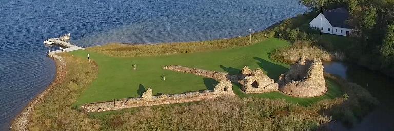 Drone photo of the beautiful ruin with castle tower and bedding. In the background you can see the jetty for the Post Boat and the white Castle House from 1945